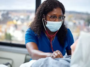 Berthine Paul, RN using a stethoscope to listen to heart of sleep apnea patient in Med 5 room at Melrose Wakefield Hospital. 